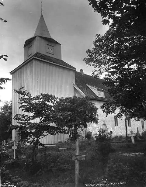 Fjære kirke sett fra kirkegården, med vesttårnet til venstre og kirkegårdskors i forgrunnen